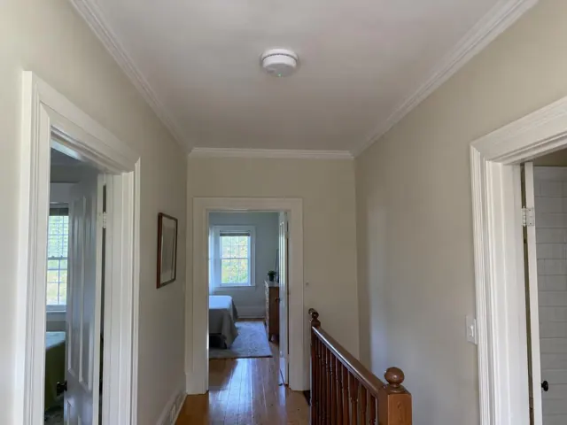 Smoke alarm on ceiling in a hallway with white walls and timber floor in Hornsby